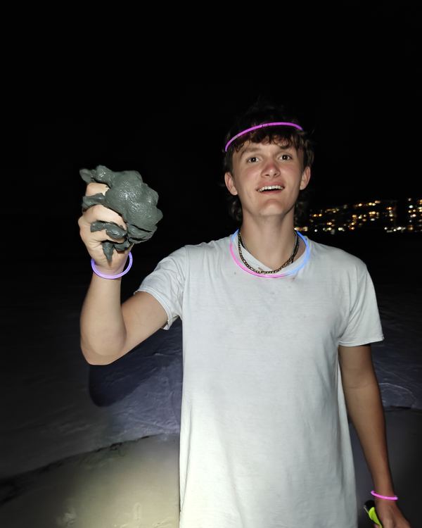A smiling guest with a glow headband holding up a big crab on the beach at night