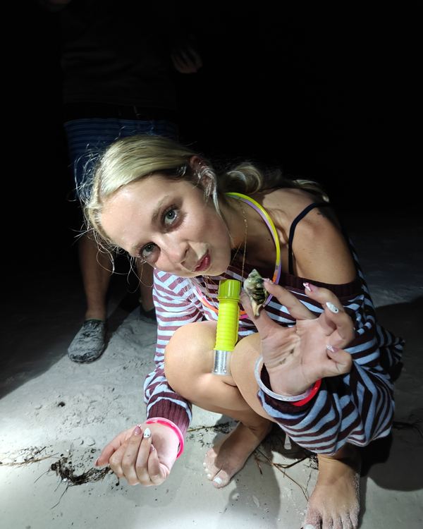 A guest crouching on the sand at night, holding out a hermit crab on her hand