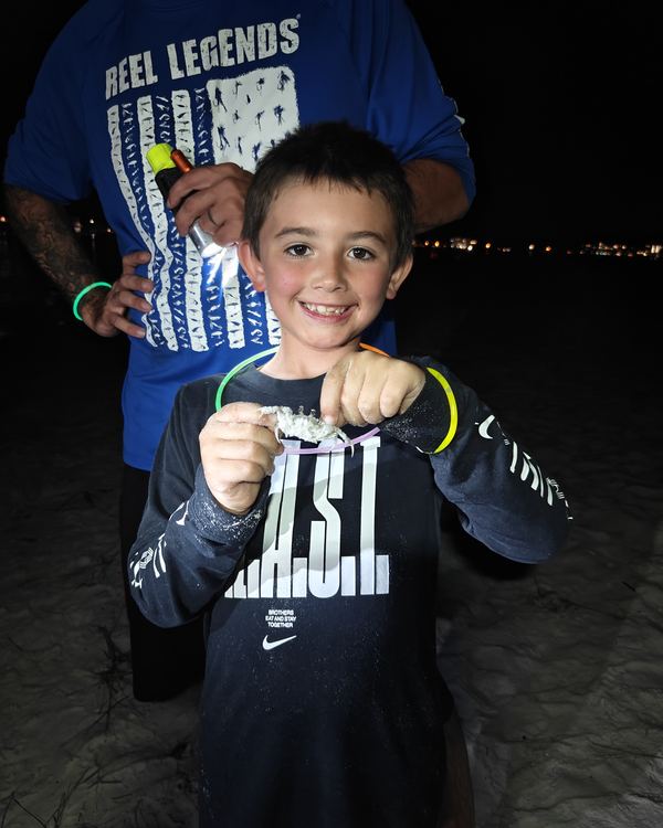 A grinning young guest holding up a crab he caught on the beach at night