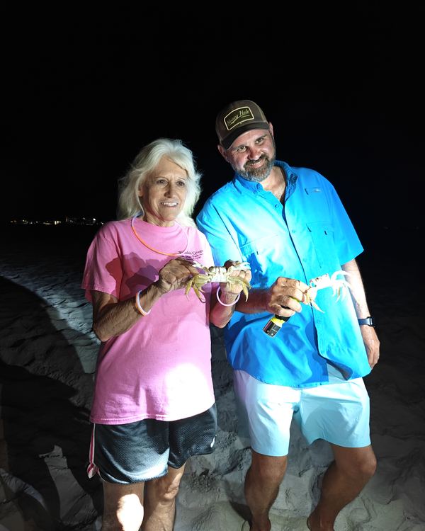 A smiling couple on the beach at night, each holding up a crab they caught on the Crab Grab tour