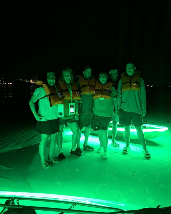 A group of guests in life jackets standing together on the island in the green kayak glow